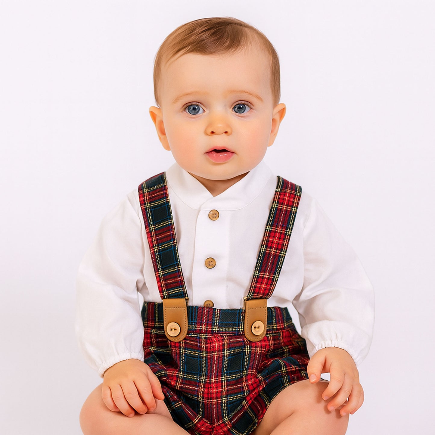 Baby wearing a white shirt with plaid braces on a light background