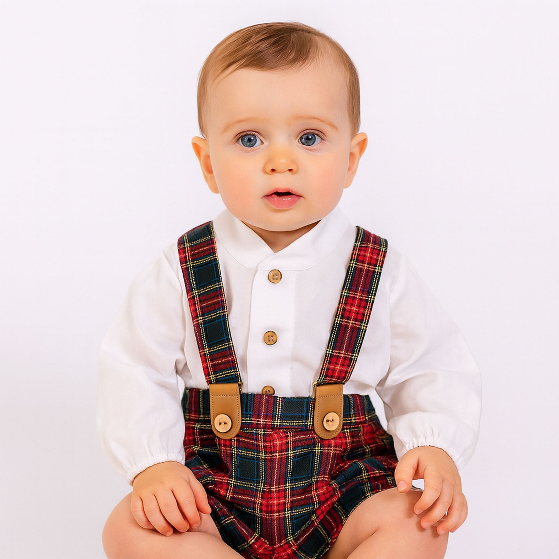Baby wearing a white shirt with plaid braces on a light background