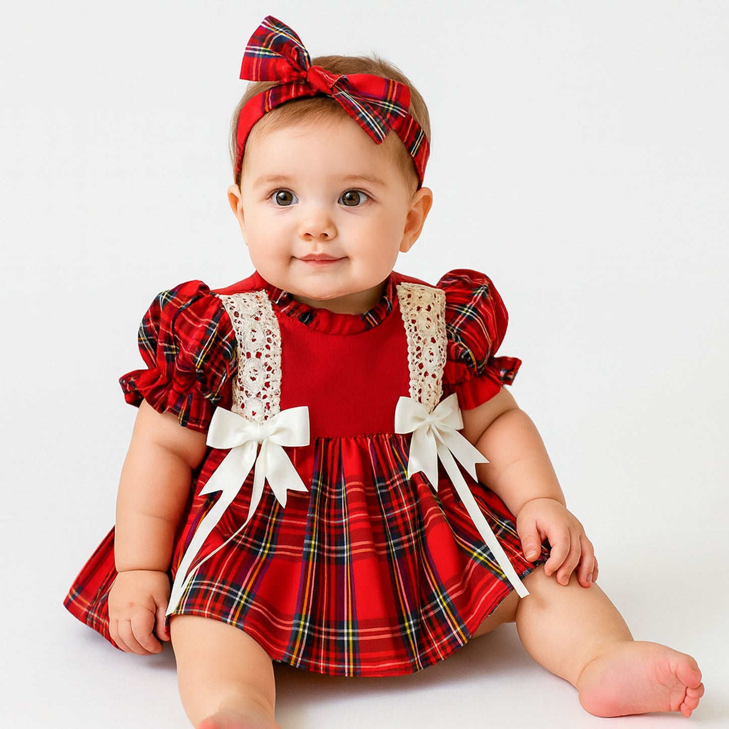 Baby wearing a red plaid dress with white bows and a matching headband on a white background