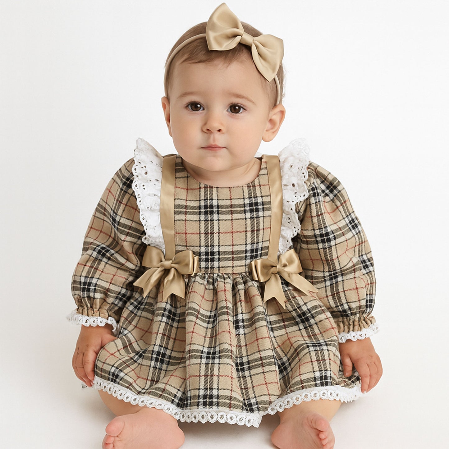 Baby wearing a plaid dress with bows and a headband on a white background