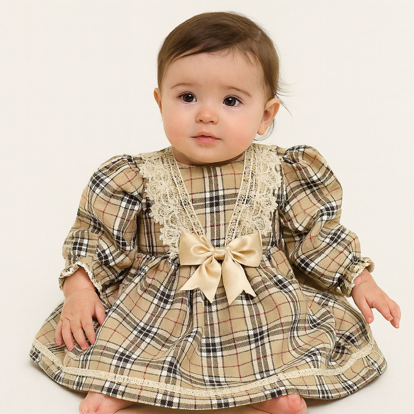 Baby wearing a plaid dress with lace details and a bow on a white background