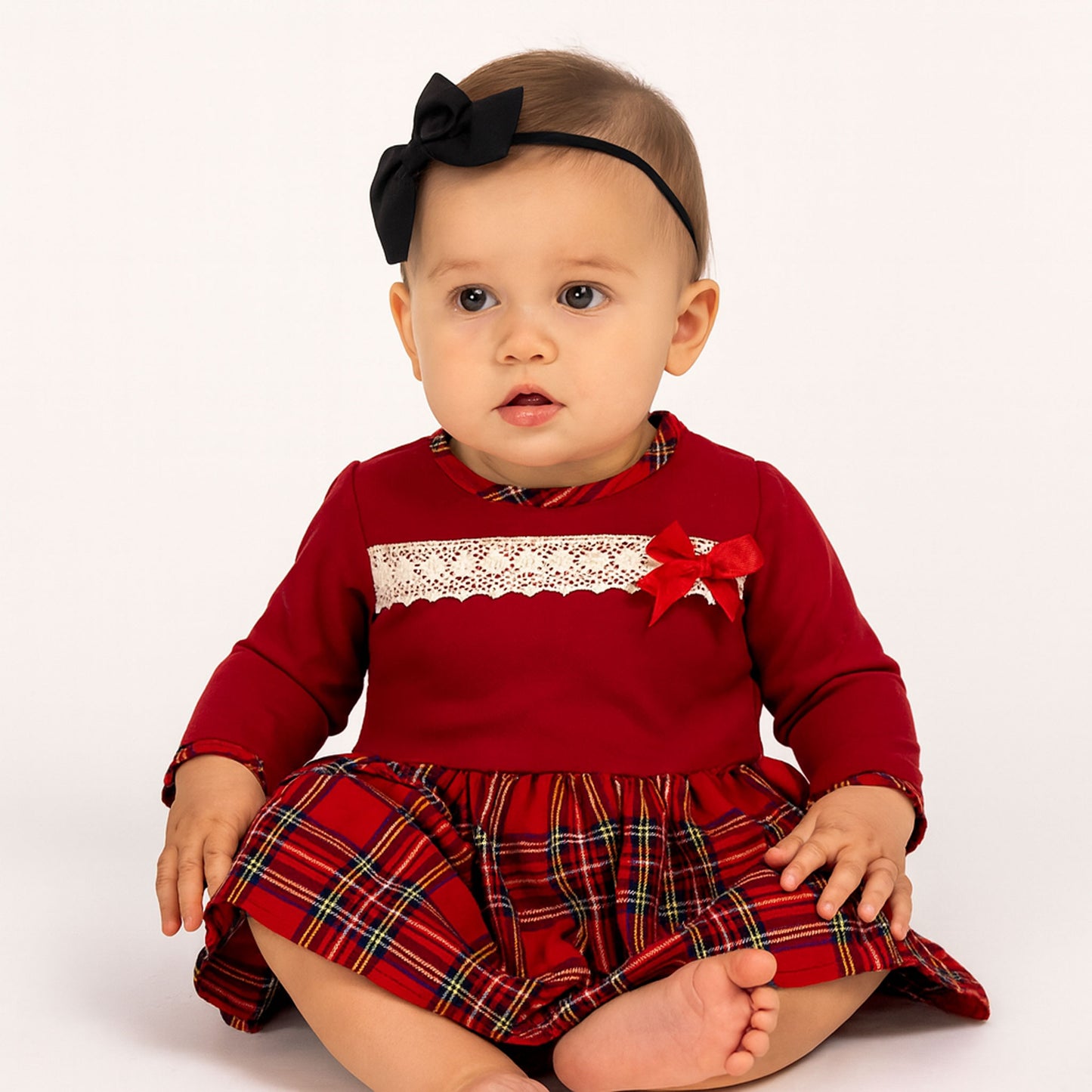 Baby wearing a red dress with plaid skirt and lace detail on a white background