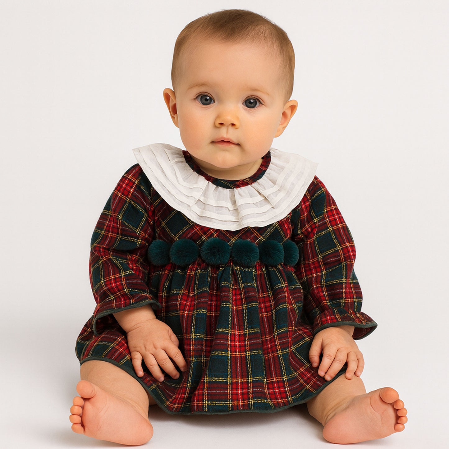 Baby wearing a red and green plaid dress with a white collar on a white background
