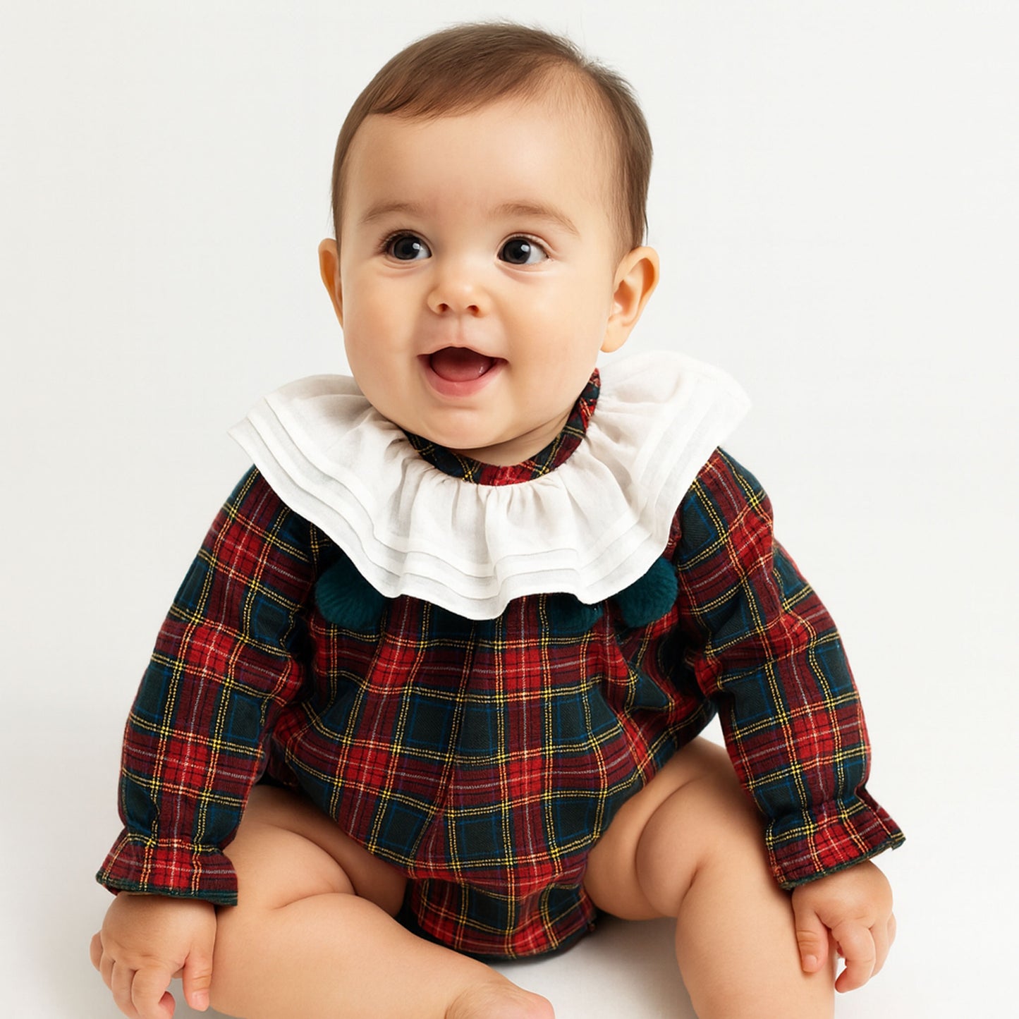 Baby wearing a plaid outfit with a white ruffled collar on a light background