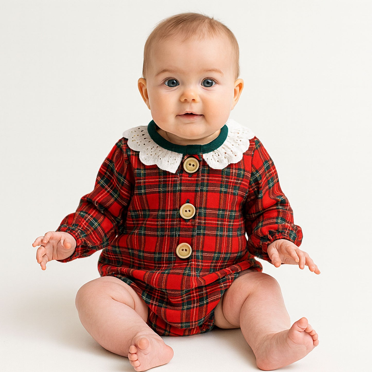 Baby wearing a red plaid outfit with a white collar on a light background