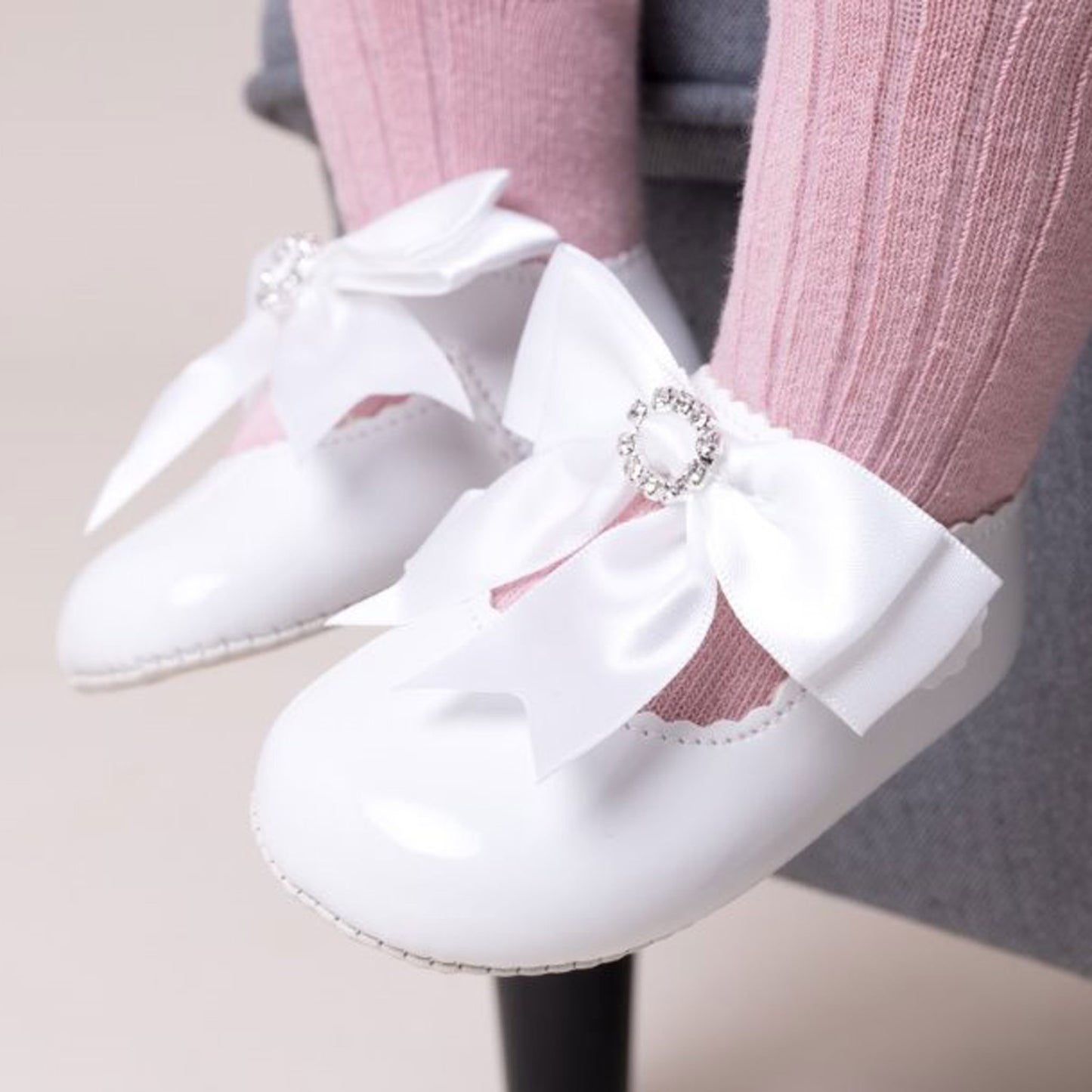 White shoes with large bows worn by a person with pink socks.