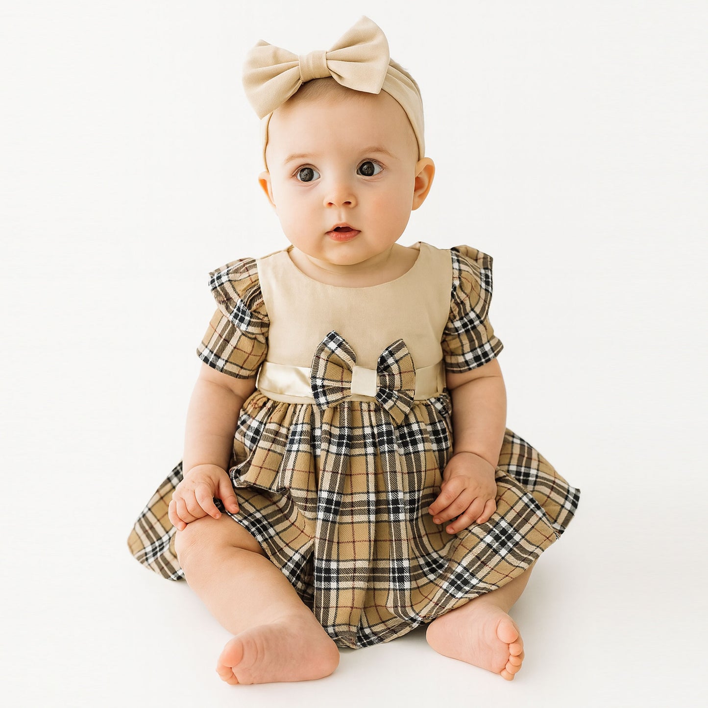 Baby wearing a plaid dress with a bow and headband on a white background