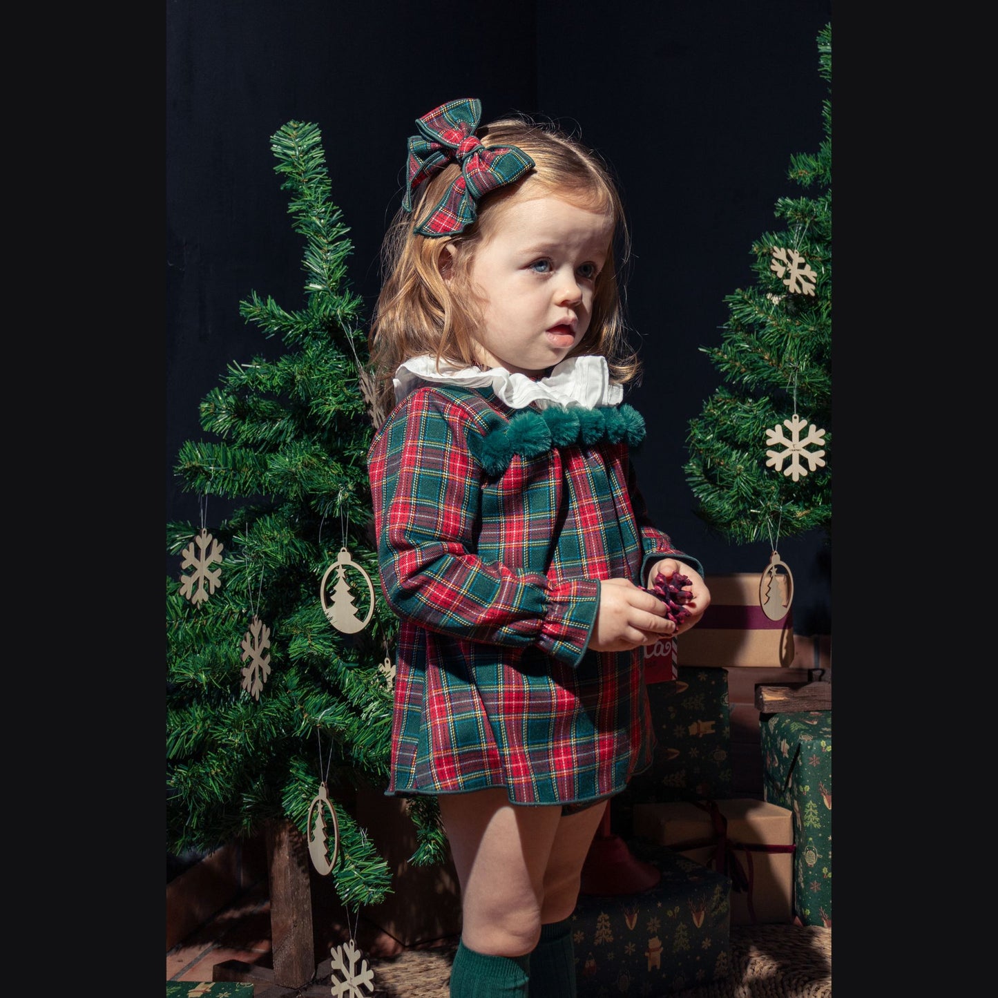 Young girl in a plaid dress standing in front of a decorated Christmas tree.