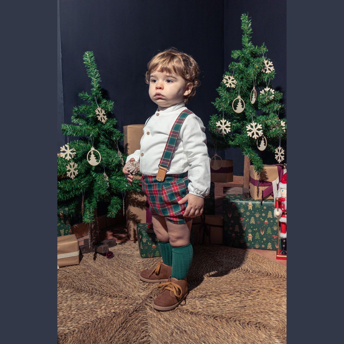 Child in festive outfit with Christmas trees and presents in the background