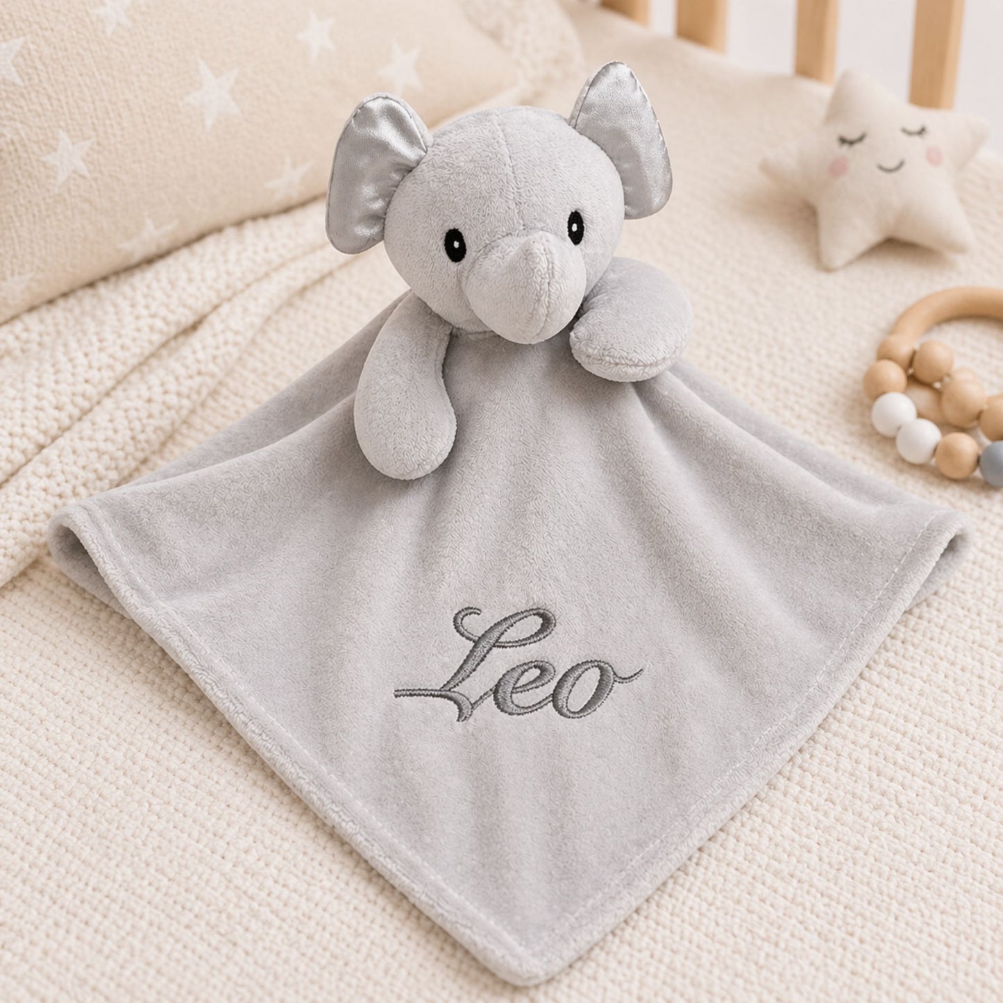 Gray elephant plush toy with blanket and 'Leo' embroidery on a crib