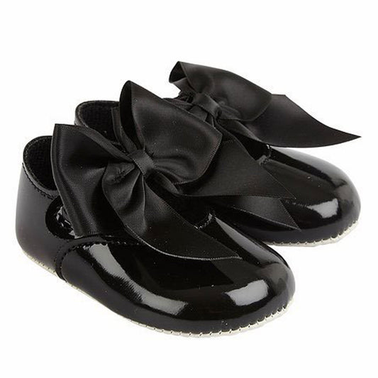 Black patent leather shoes with large bows on a white background