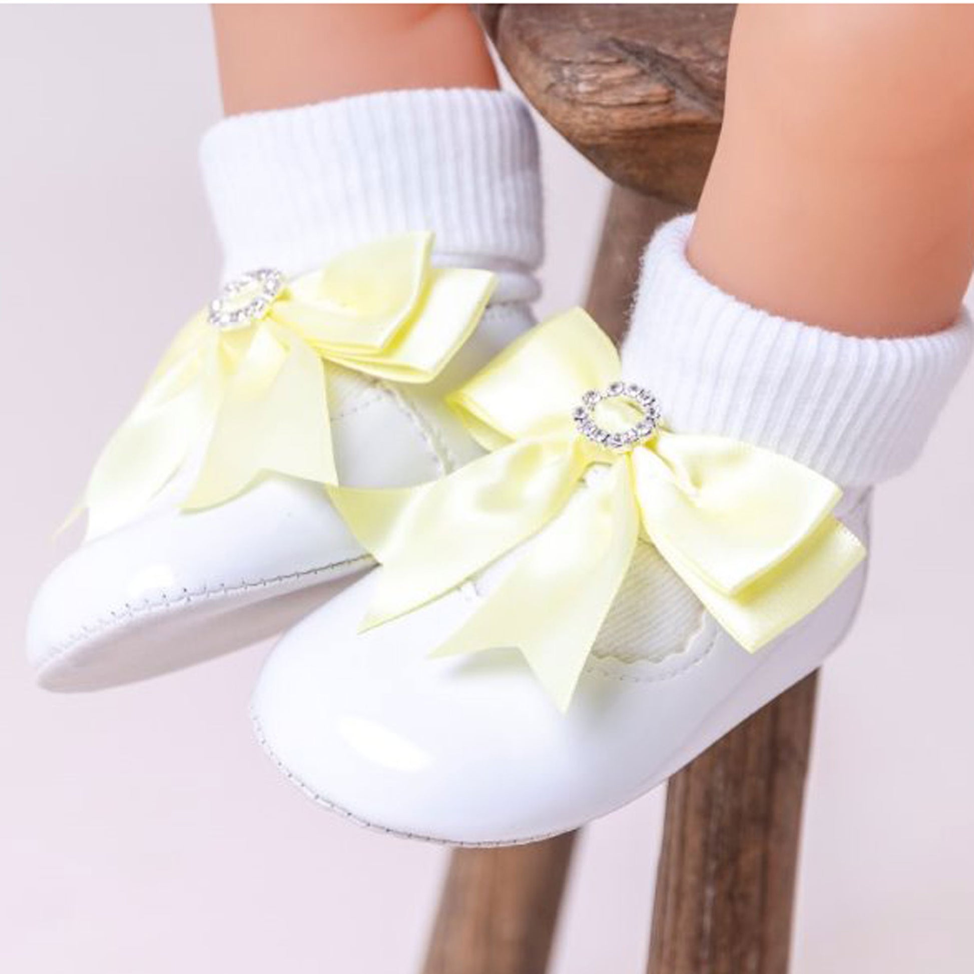 White baby shoes with yellow bows and rhinestones on a light background