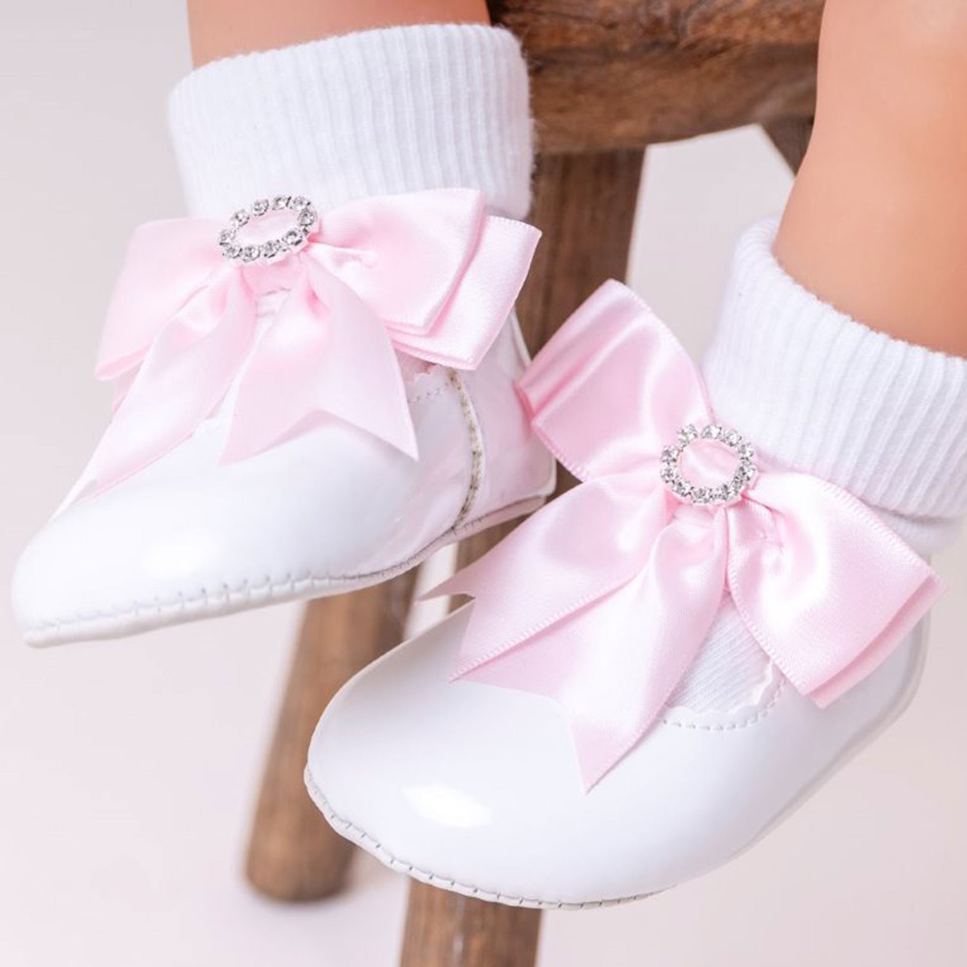 White shoes with pink bows and rhinestones on a neutral background