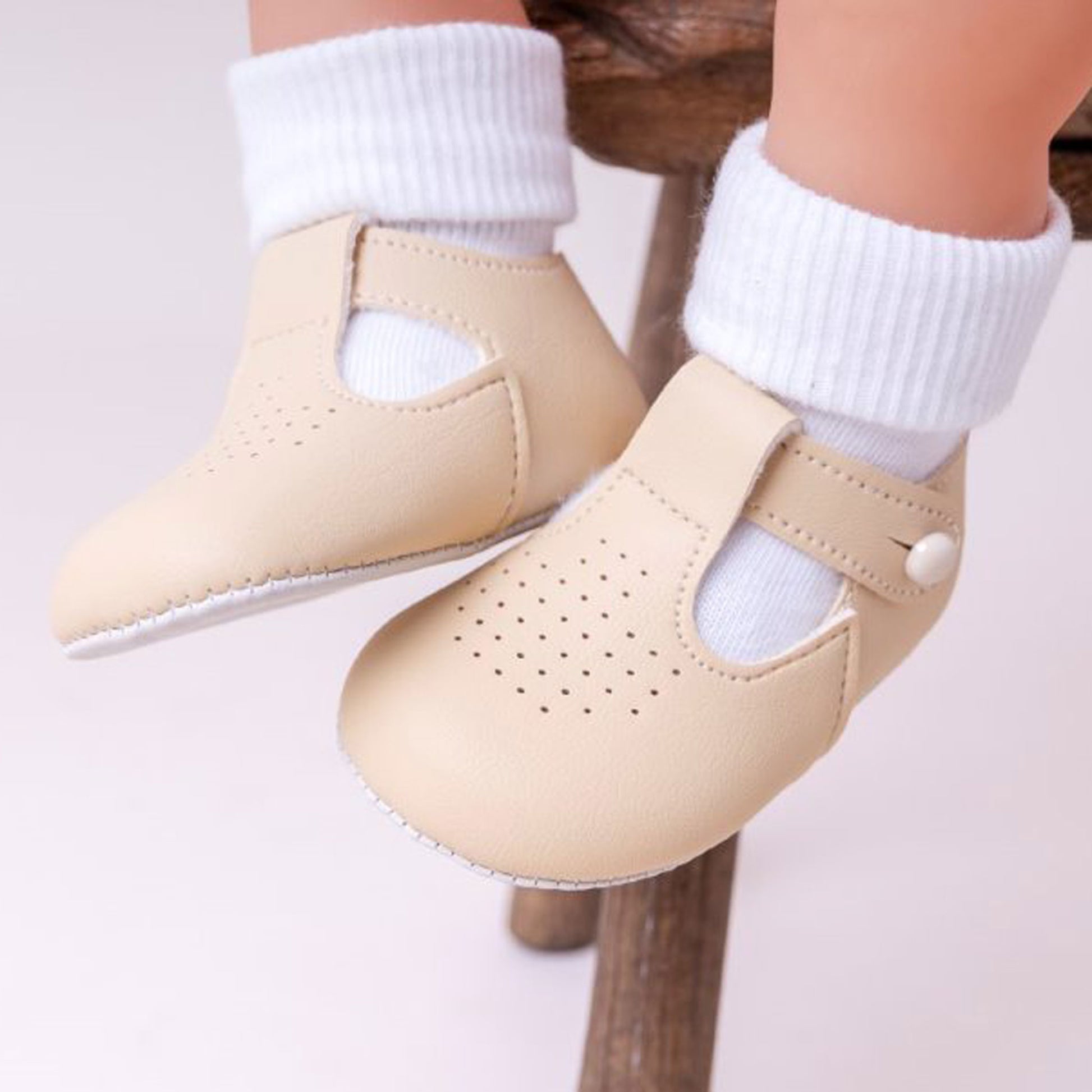 Beige baby shoes with white socks on a neutral background