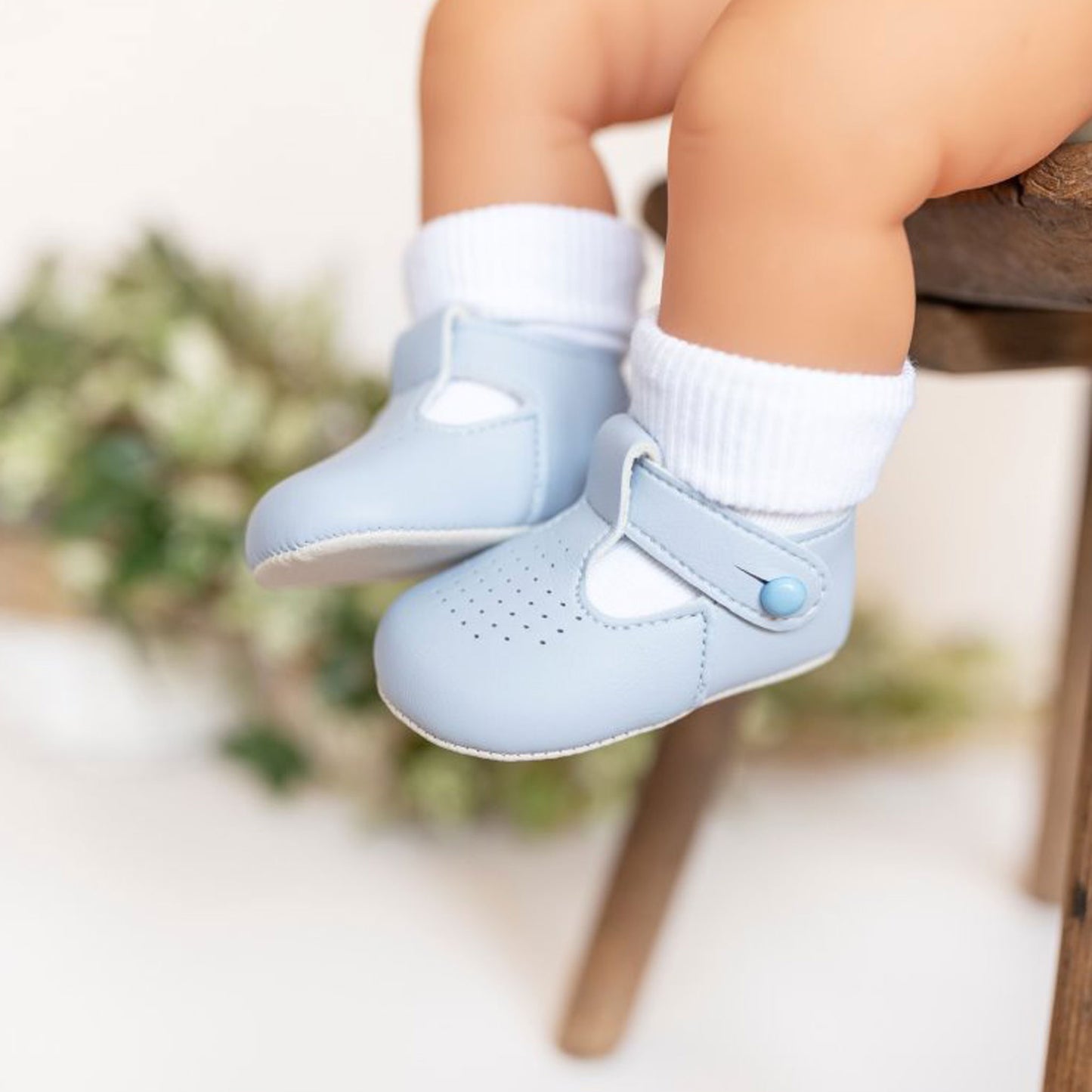 Baby's feet wearing light blue shoes with white socks against a blurred natural background