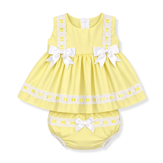 Yellow baby dress with white lace and bows on a white background