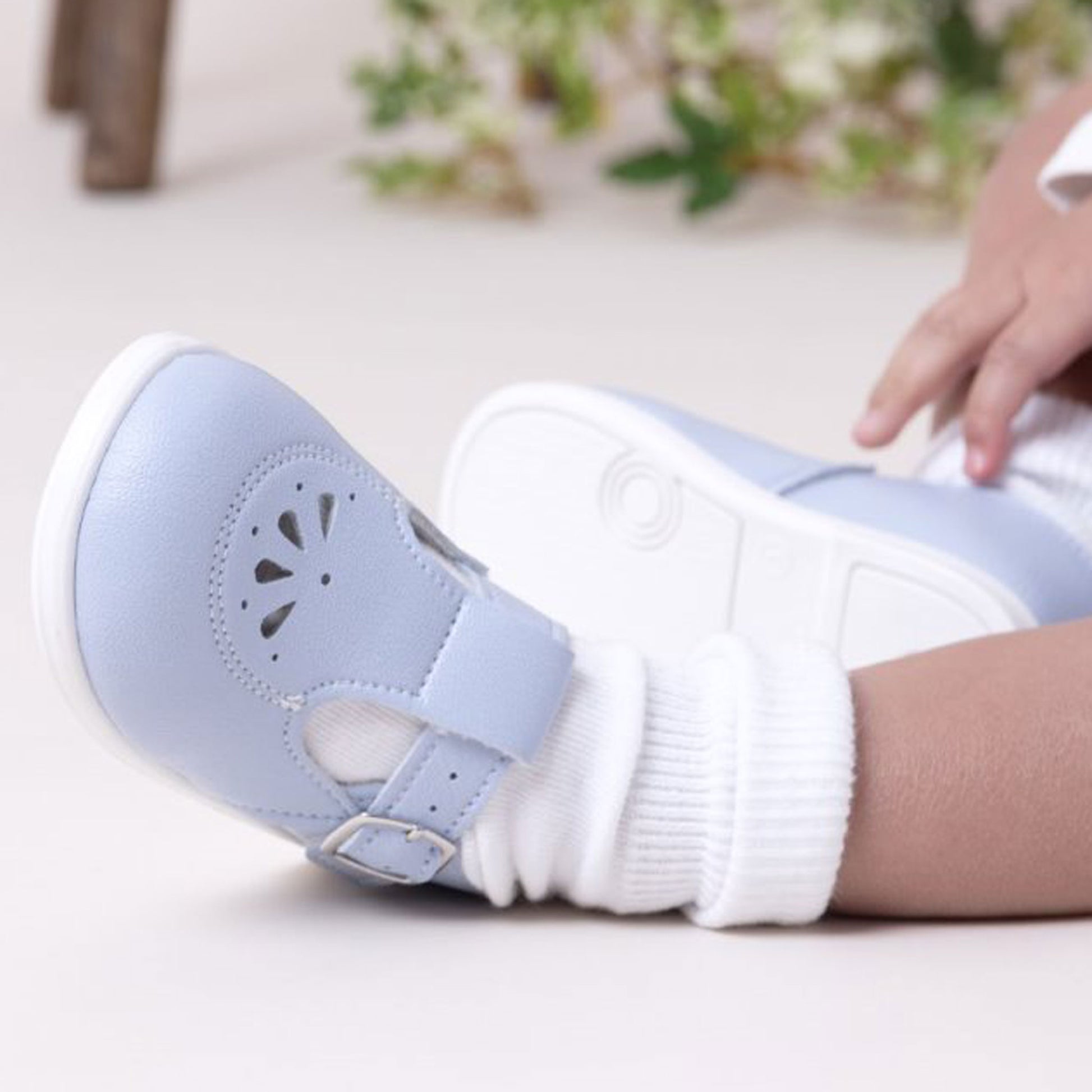 Child's foot wearing a light blue sandal with a white sole on a light background.