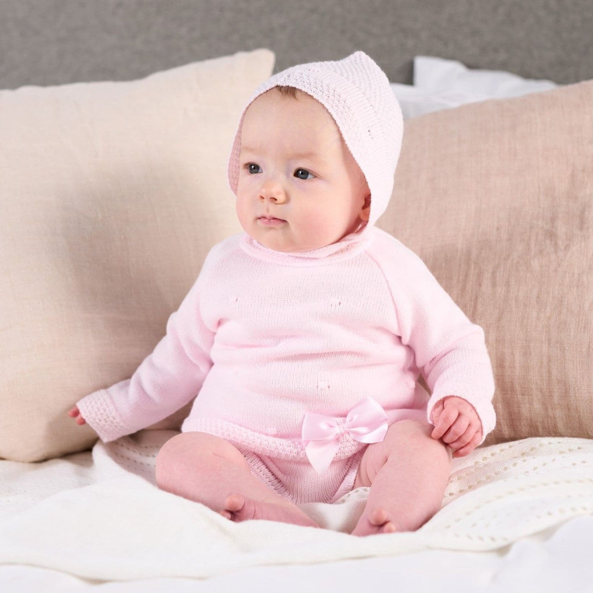 Baby in a pink outfit sitting on a couch