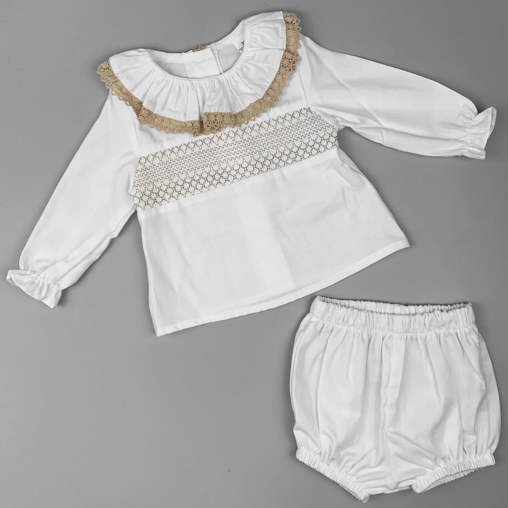 A stylish and cozy baby girl’s white outfit, featuring a lace-trimmed collar and smocked design