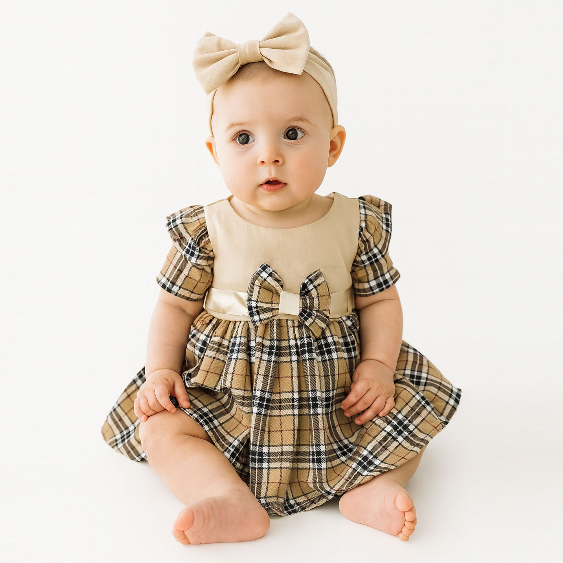 Baby wearing a plaid dress with a bow and headband on a white background