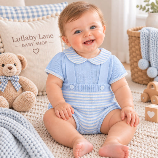 A baby sitting on a cream carpet wearing a light blue and white striped short-sleeve romper with a Peter Pan collar. The background features a cozy nursery setting with a teddy bear, a pillow reading 'Lullaby Lane BABY SHOP', and soft toys.