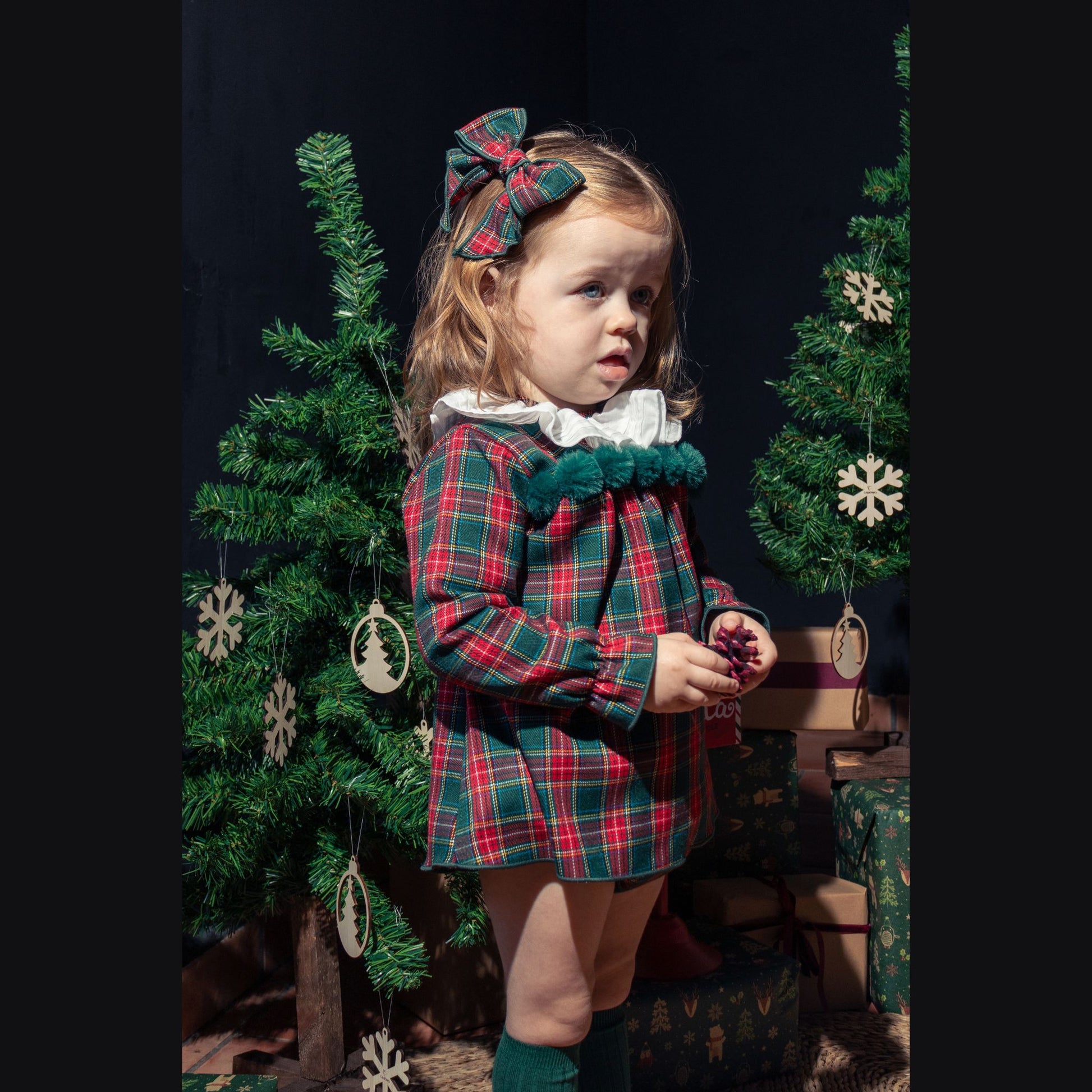 Young girl in a plaid dress standing in front of a decorated Christmas tree.