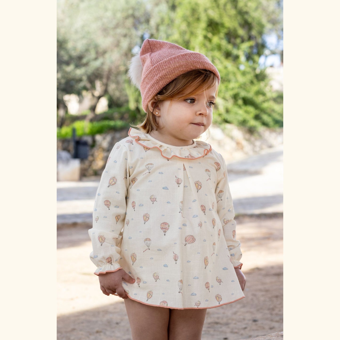 Child wearing a patterned dress and pink beanie outdoors