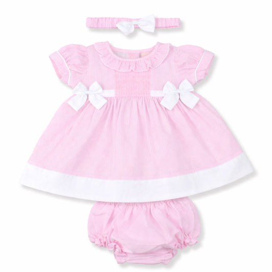 Pink baby dress with white bows, bloomers, and headband on a white background