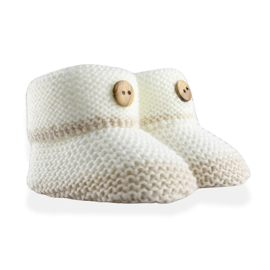 Pair of white knitted baby booties with wooden buttons on a white background