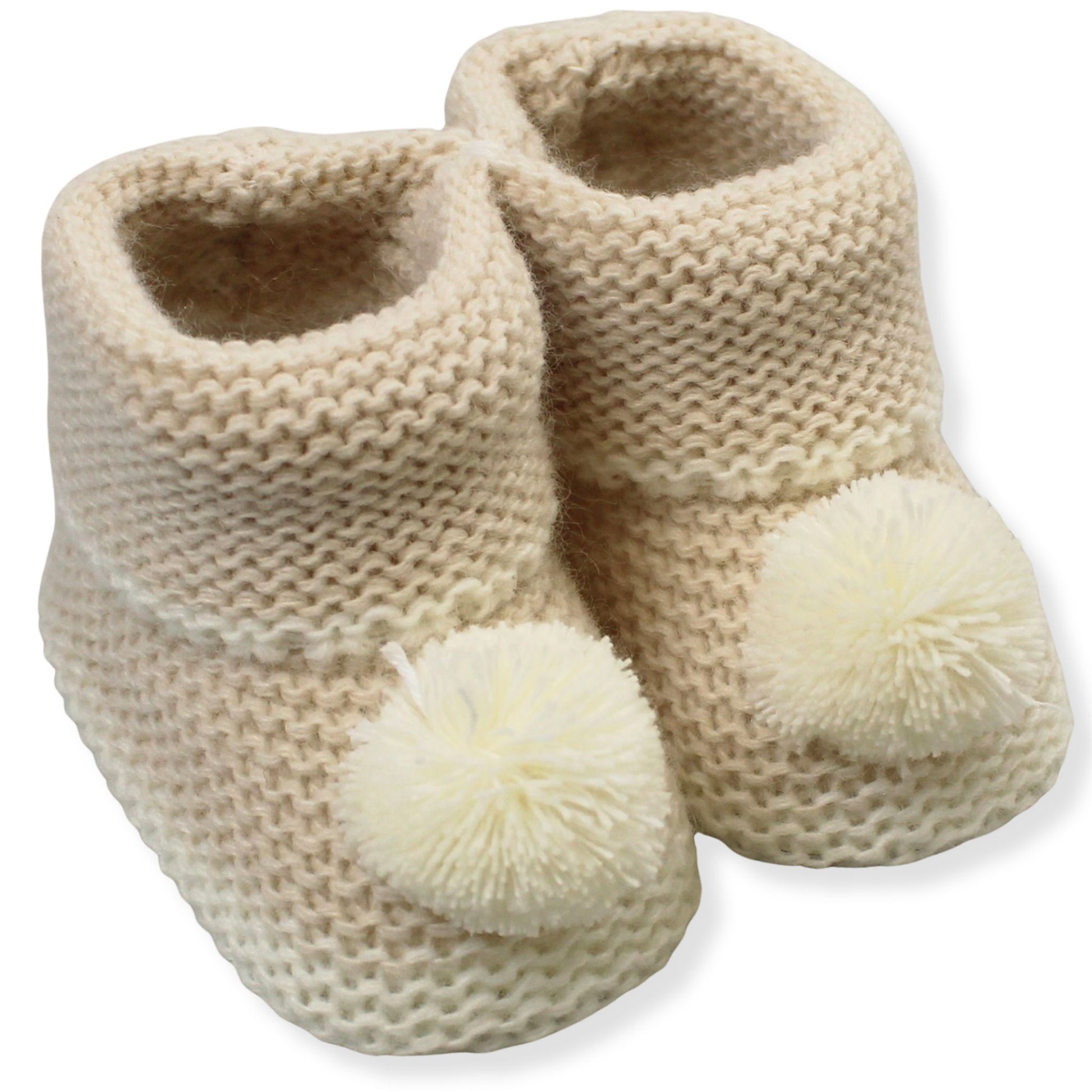 Pair of beige knitted baby booties with pom-poms on a white background
