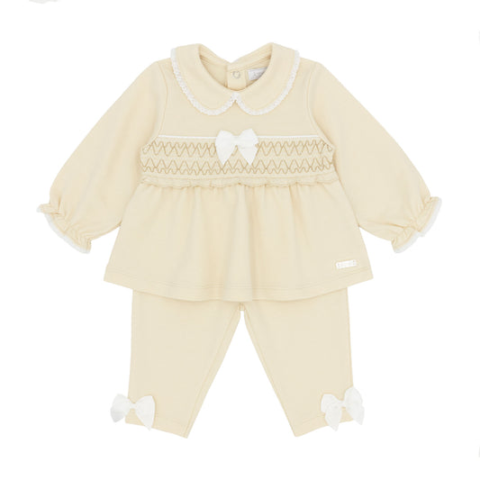 A baby girl's two-piece knit outfit set in beige, featuring a long-sleeve smocked top with a Peter Pan collar and matching pants with bow details.