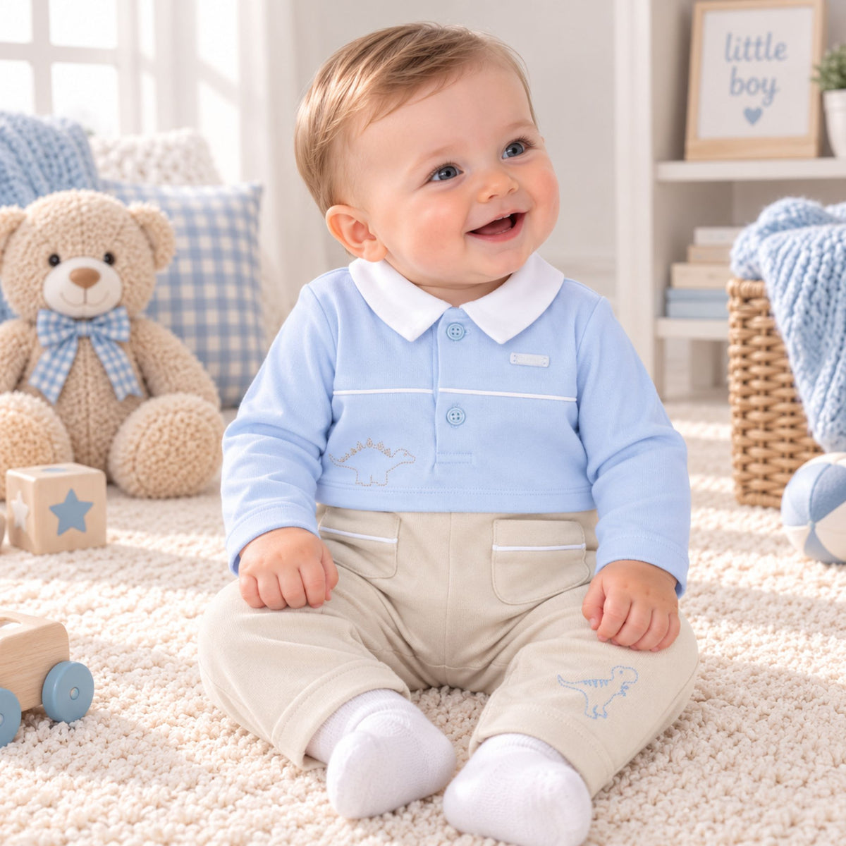 A baby sitting on a cream carpet in a bright nursery, wearing a light blue long-sleeve polo shirt with a white collar and beige pants with white socks.