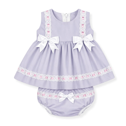 Lavender baby dress with white bows and lace details on a white background