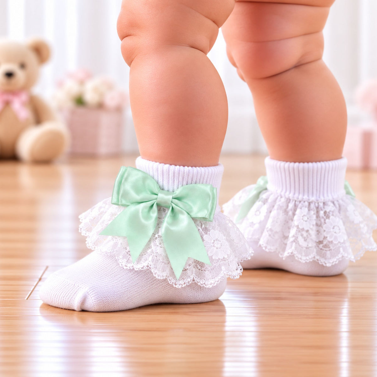 White baby socks with ruffled lace and a mint green satin bow, shown on a baby's feet on a wooden floor.
