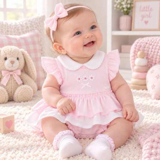 A baby girl sitting on a fluffy cream carpet in a cozy nursery, wearing a light pink ruffled dress with a white Peter Pan collar, a matching pink bow headband, and white socks.