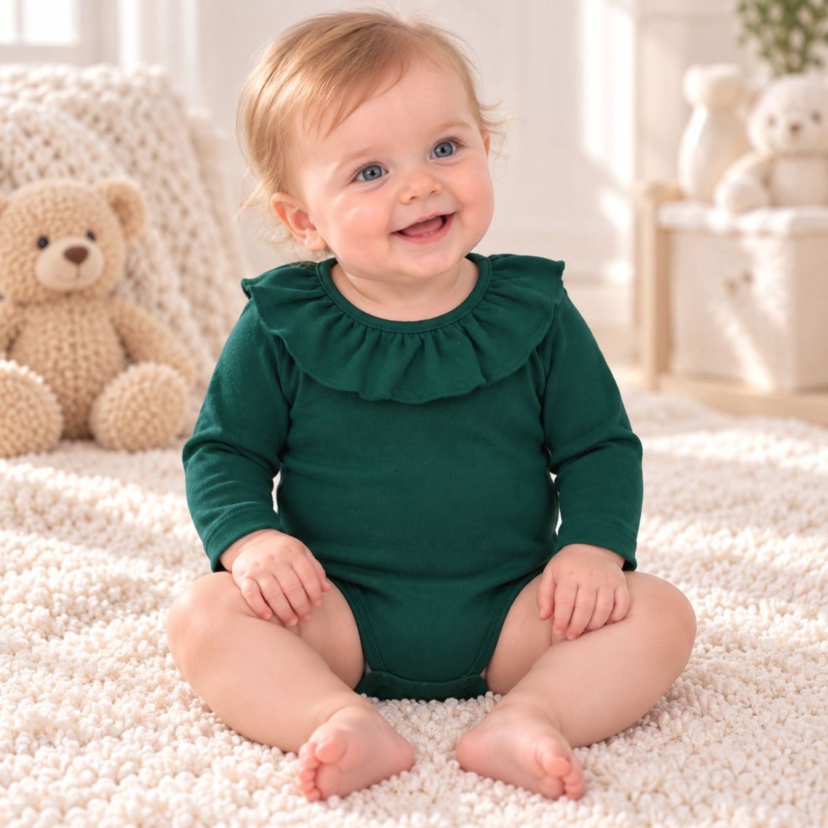 A baby sitting on a white textured rug wearing a dark green long-sleeve romper with a ruffled collar, surrounded by soft toys in a bright indoor setting.