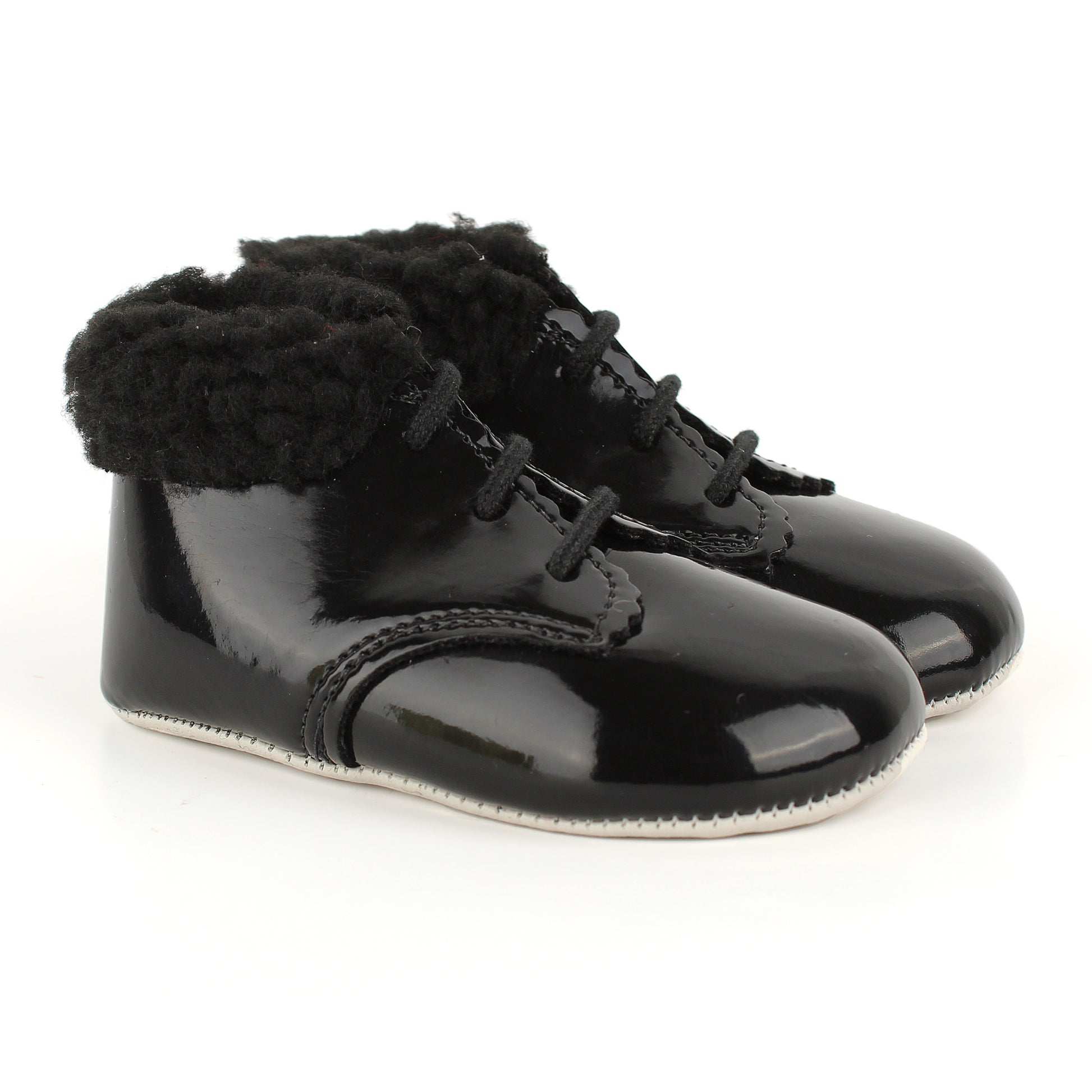 A pair of black patent leather baby booties with fluffy black faux-fur trim around the collar and black laces, shown on a white background.