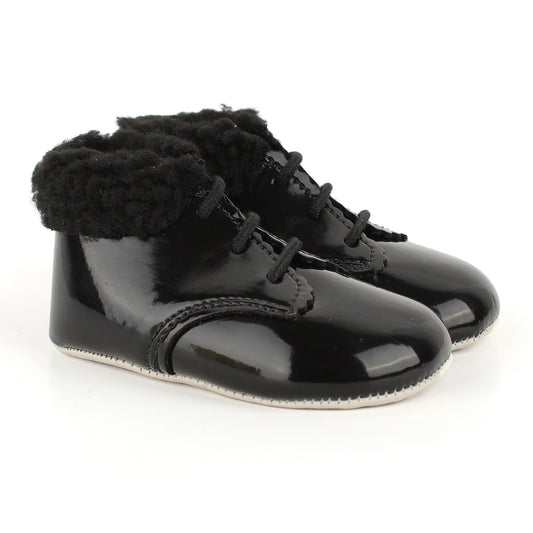 A pair of black patent leather baby booties with fluffy black faux-fur trim around the collar and black laces, shown on a white background.