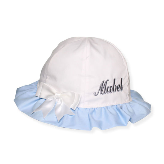 White baby hat with blue trim and a bow, featuring the name 'Mabel' on a white background.