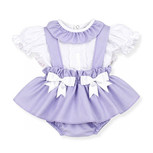 lilac baby outfit with white ruffled top and bow details on a white background