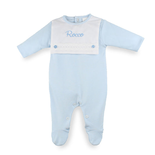 A light blue baby footed sleepsuit with a white bib panel on the chest, personalized with the name Rocco in blue embroidery.