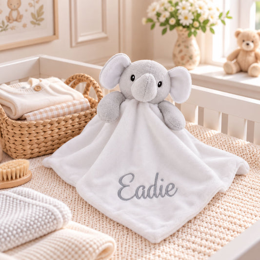A personalized white baby comforter featuring a plush gray elephant head and the name 'Eadie' embroidered in gray script, styled in a soft, neutral nursery setting.