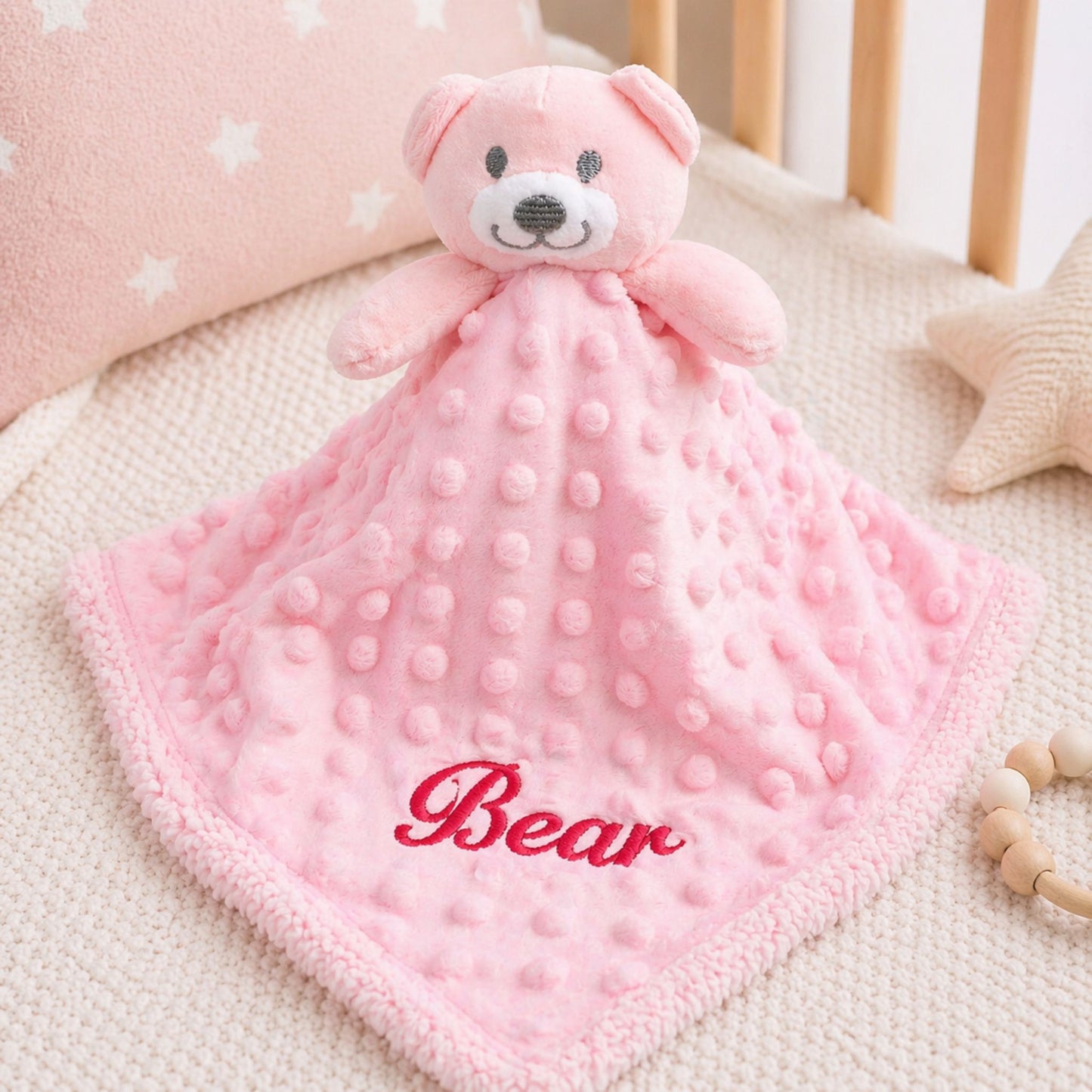 Pink teddy bear security blanket with 'Bear' embroidery on a crib