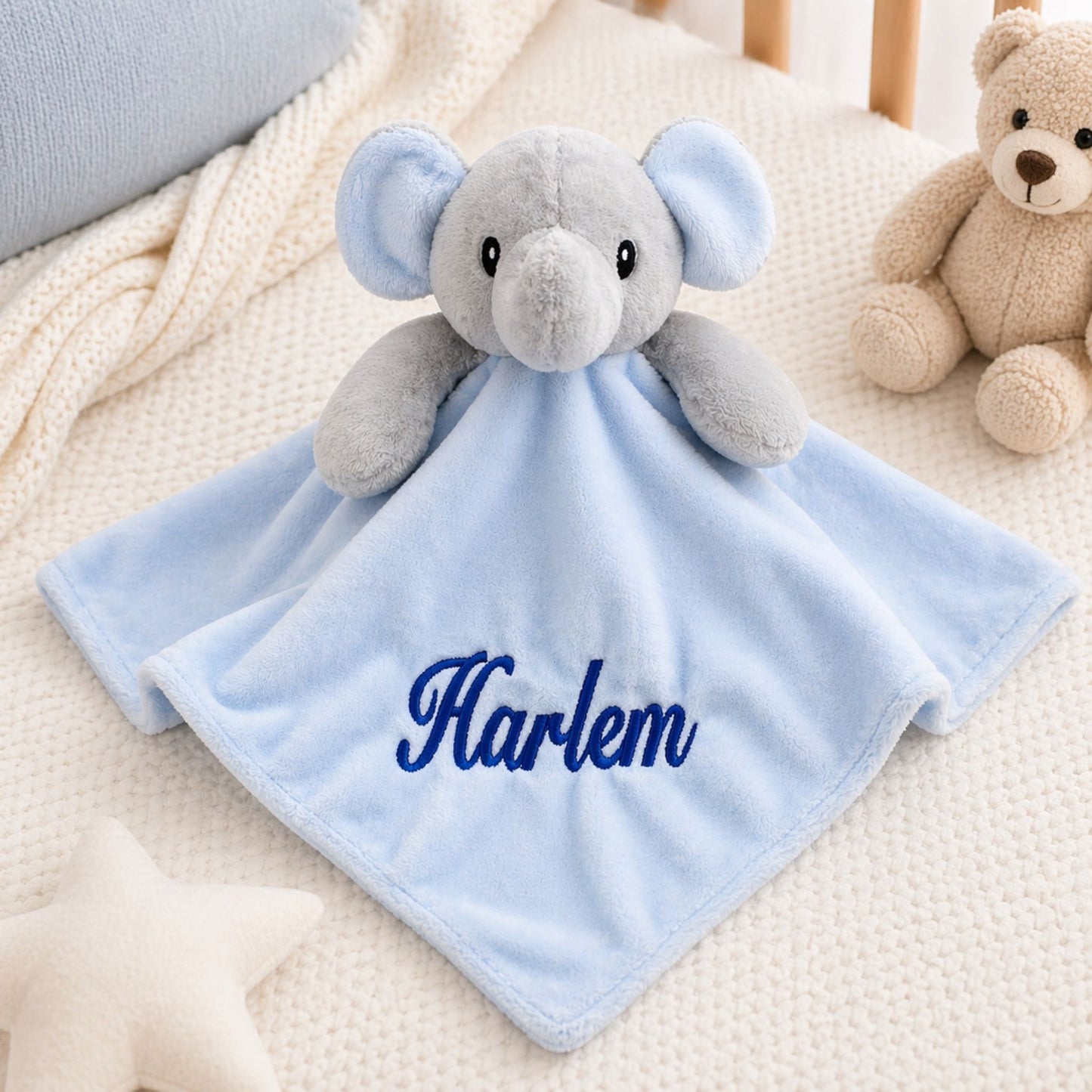 Gray elephant plush toy with a blue blanket displaying 'Harlem' on a soft surface.
