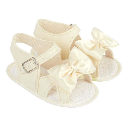 Pair of cream-colored baby sandals with large bows on a white background