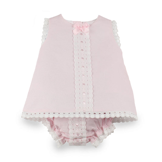 A baby girl's two-piece outfit in light pink textured fabric, featuring a sleeveless top with white scalloped lace trim and a matching pink ruffled bloomers set with lace trim, accented by a small pink bow at the neckline.