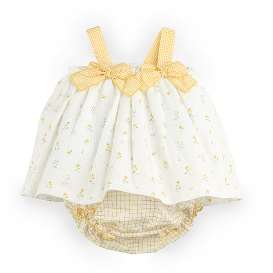 A baby romper in white muslin fabric with a small yellow floral print, featuring yellow gingham checkered straps and bows, and a matching yellow gingham diaper cover underneath.