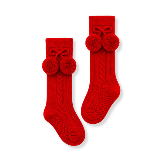 A pair of bright red cable-knit baby socks with pom-pom bows on the cuff, displayed on a clean white background.