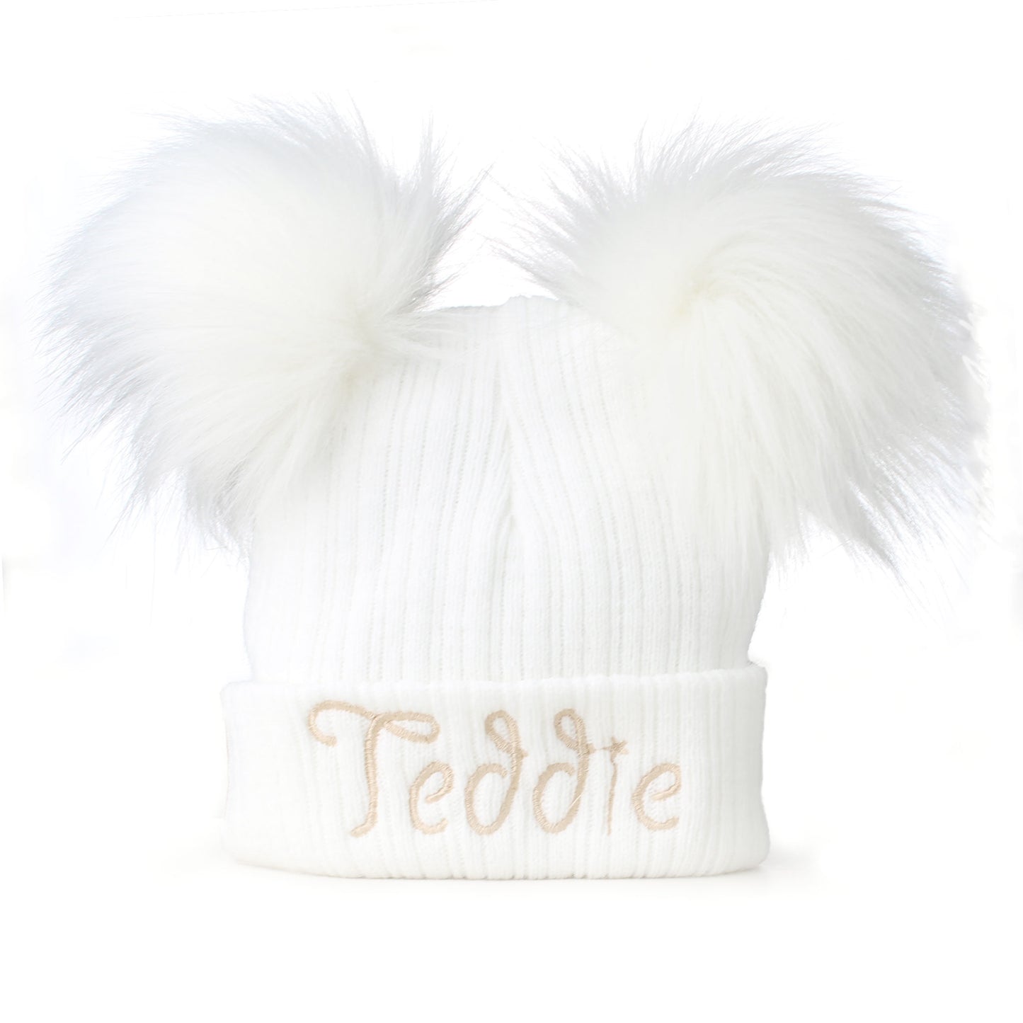 White knit beanie with fluffy pom-poms and 'Teddie' embroidery on a white background