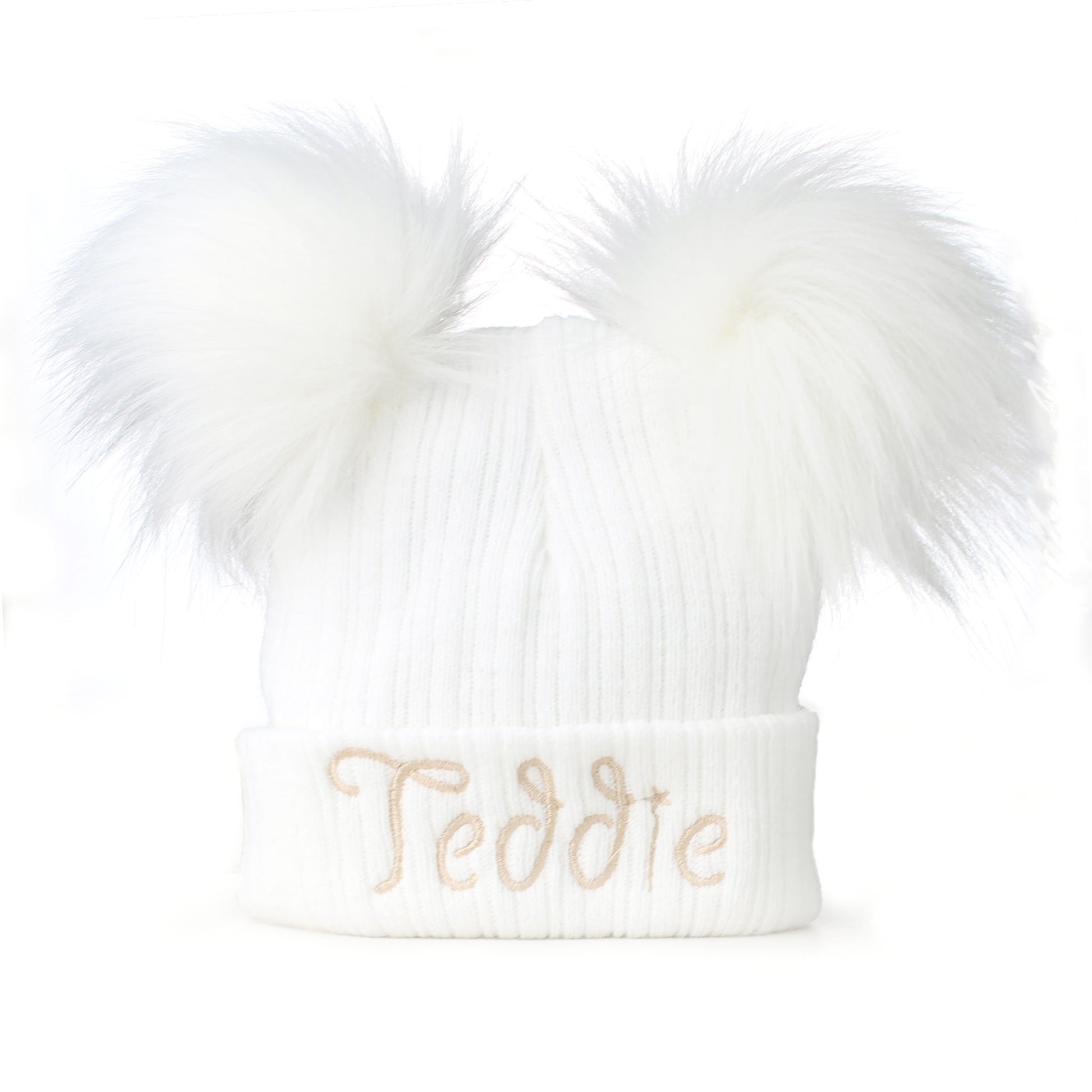 White knit beanie with fluffy pom-poms and 'Teddie' embroidery on a white background